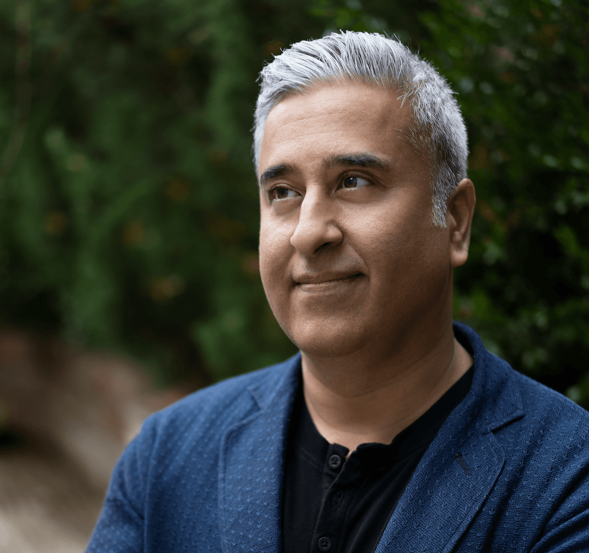 Professionally dressed man with gray hair in outdoor setting looks off to the left