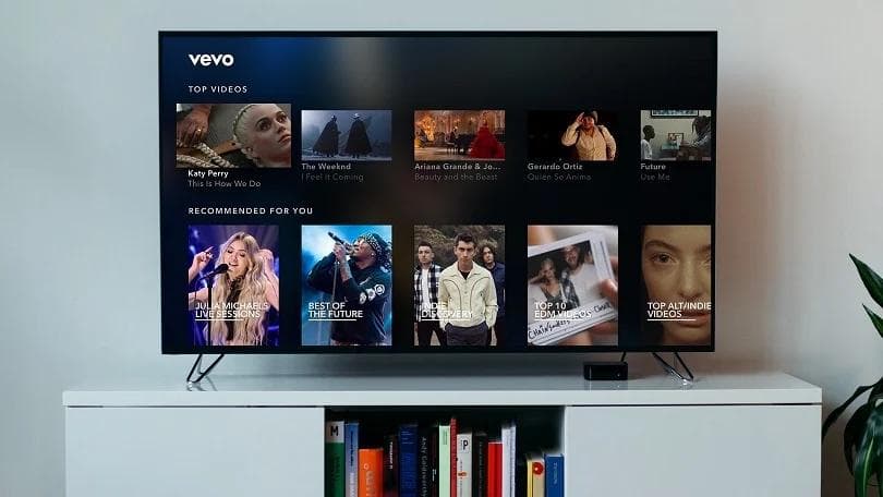 TV sits atop a bookcase in spare white room. Screen displays the Vevo interface with "top videos" and "recommended for you".